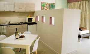 En lejlighed med et køkken med bordplade, skabe, mikrobølgeovn og køleskab. Et hvidt spisebord med stole står i forgrunden. (AI-genereret tekst)