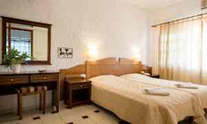 Et hotelværelse med to separate senge, en trækommode og hvide vægge. (AI-genereret tekst)