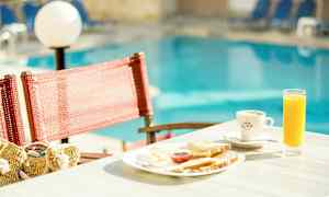 En morgenmadstallerken med juice og kaffe på et bord ved en pool. (AI-genereret tekst)