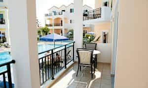 En balkon med møbler, udsigt over en pool og orange bygninger. (AI-genereret tekst)