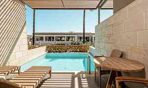 En privat terrasse med liggestole, et bord og pool, med udsigt til en bygning i det fjerne. (AI-genereret tekst)