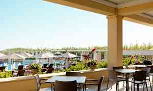 Udendørs serveringsområde med stole og borde og udsigt til en pool og solsenge. (AI-genereret tekst)