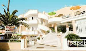 Bygning med hvid facade og vindeltrappe, omgivet af grønt og med et skilt, der viser 'Rita Suites'. (AI-genereret tekst)