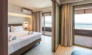 Hotelværelse med seng og håndklæder, store glasdøre der fører ud til en balkon med havudsigt. (AI-genereret tekst)