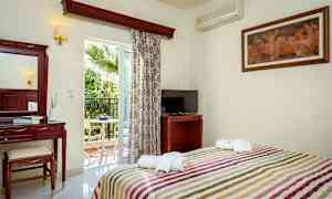 Et hotelværelse med seng, TV, makeupbord og altan med udsigt til en palme. (AI-genereret tekst)