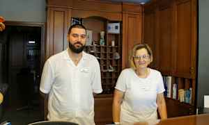 To personer står ved en receptionsdisk med træpaneler i baggrunden. (AI-genereret tekst)