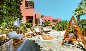 Liggestole og parasoller på en stenlagt terrasse med en lyserød bygning i baggrunden. (AI-genereret tekst)