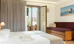 Et hotelværelse med to senge med lyse lagner, en lilla sofa med puder og en glasdør, der fører ud til en balkon. (AI-genereret tekst)