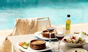 Tallerkener med græske retter, to glas rødvin og en pool i baggrunden. (AI-genereret tekst)
