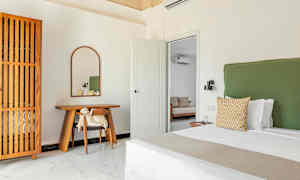 Et soveværelse med en grøn sengegavl, et skrivebord af træ med et spejl ovenover og et trædetaljeret garderobeskab. (AI-genereret tekst)