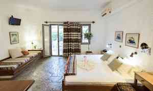 Et hotelværelse med en seng, siddebænk, bord og en dør, der fører til en altan. (AI-genereret tekst)