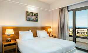 Et værelse med to enkeltsenge, bordlamper og en vinduesdør, der vender ud mod havet. (AI-genereret tekst)