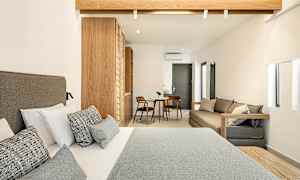 Hotelværelse med en dobbeltseng i forgrunden, træindretning og et mindre siddeområde med bord og to stole i baggrunden. (AI-genereret tekst)