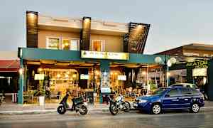 Facade af Akatos Hotel med biler og motorcykler parkeret foran. (AI-genereret tekst)