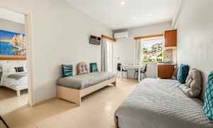 Et hotelværelse med to enkeltsenge, et bord og stole samt udsigt gennem vinduet. (AI-genereret tekst)