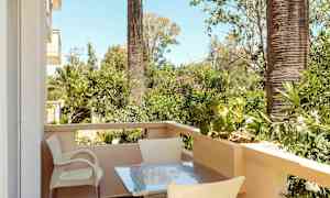 En altan med bord og stole, omgivet af grønne planter og palmer. (AI-genereret tekst)