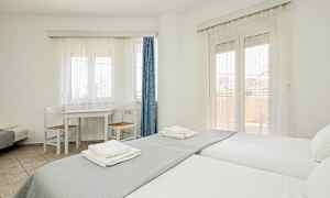 Et lyst værelse med to enkeltsenge, et bord med to stole og vinduer dækket med hvide gardiner. (AI-genereret tekst)