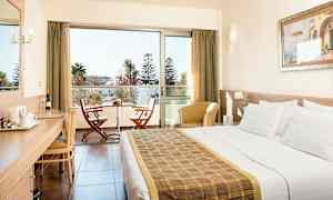 Hotelværelse med dobbeltseng, skrivebord, siddepladser og en balkon med to stole og et bord. (AI-genereret tekst)