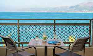 To stole ved et bord med en karaffel og to glas, med udsigt over havet. (AI-genereret tekst)