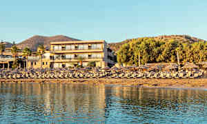 Et ferieanlæg ved stranden med liggestole og parasoller i forgrunden og et hotel bagved. (AI-genereret tekst)