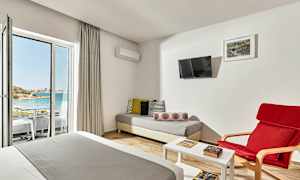 Et hotelværelse med siddeområde, seng og udsigt til en strand gennem en glasdør. (AI-genereret tekst)