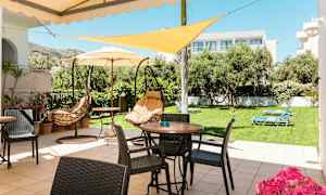 En terrasse med borde, stole og hængesofaer, omgivet af en græsplæne med solsenge og træer. (AI-genereret tekst)