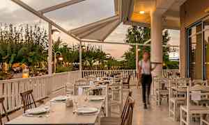 Udendørs servering med dækkede borde under tag, omgivet af grønne omgivelser. (AI-genereret tekst)