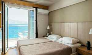 Et hotelværelse med to enkeltsenge og en åben altandør, der vender ud mod havet. (AI-genereret tekst)