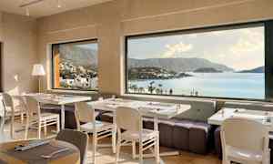 Restaurant med dækkede borde og panoramaudsigt over kyst og bjerge. (AI-genereret tekst)