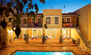 Lejlighedskompleks med en pool i forgrunden, omgivet af terrakottafarvede bygninger og beplantning. (AI-genereret tekst)