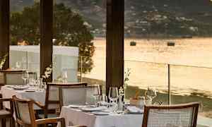 En udendørs restaurant med dækkede borde ved vandet og udsigt over havet. (AI-genereret tekst)