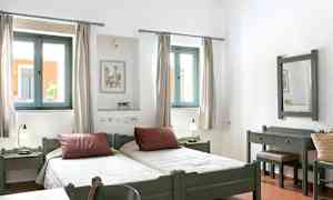 Billede af et lyst soveværelse med to enkeltsenge, vinduer med lysindfald og træmøbler. (AI-genereret tekst)