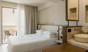 Indretning af et hotelværelse med en dobbeltseng, et vindue med gardiner, en balkon med stol og en vask. (AI-genereret tekst)