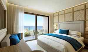 Et hotelværelse med en dobbeltseng, sofa og udsigt over havet fra en balkon. (AI-genereret tekst)