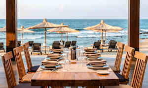 Et dækket bord med tallerkener og glas, med udsigt over stranden og havet. (AI-genereret tekst)