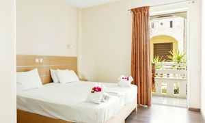 Et lyst hotelværelse med en dobbeltseng redt med hvide lagner og pyntedetaljer. Værelset har et vindue med gardin og udsigt til en altan. (AI-genereret tekst)