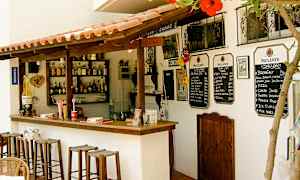 En lille udendørs bar med træstole, drikkeflasker på hylderne og menuer på væggen. (AI-genereret tekst)