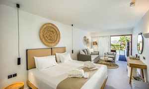 Et moderne hotelværelse med en stor seng, siddeområde og udsigt til en pool gennem glasdøre. (AI-genereret tekst)