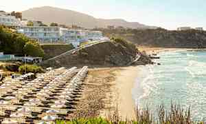 Strand med liggestole og parasoller, bygninger på skråningen. (AI-genereret tekst)