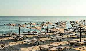 Strand med liggestole og parasoller ved havet. (AI-genereret tekst)