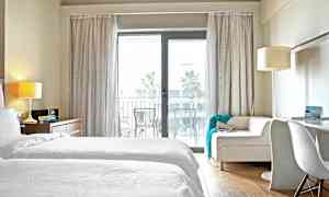 Et hotelværelse med hvidt sengetøj og en sofa foran en glasdør til en altan. (AI-genereret tekst)