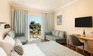 Et hotelværelse med en stor seng, siddegruppe og et skrivebord. Terrassen kan ses gennem glasdøre. (AI-genereret tekst)