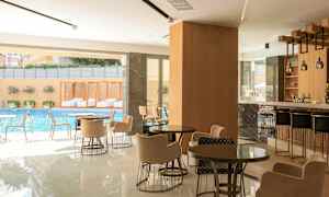 Et moderne caféområde med siddegrupper, en bar og udsigt til en swimmingpool udenfor. (AI-genereret tekst)