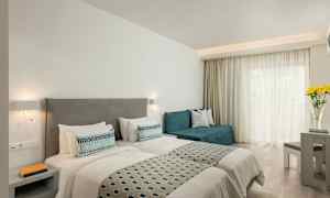 Et hotelværelse med to enkeltsenge, en sofa, et bord og blomster på et bord ved et vindue. (AI-genereret tekst)