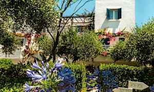 En hvid bygning med blå skodder og blomstrende planter i haven. (AI-genereret tekst)