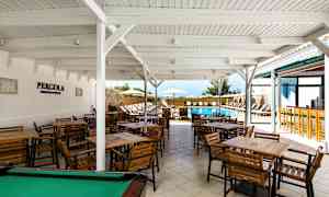 Udendørs servering med flere træborde og stole under et hvidt tag tæt på en udendørs swimmingpool. (AI-genereret tekst)