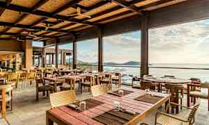 En åben og lys restaurant med træborde og stole, med udsigt over havet og horisonten. (AI-genereret tekst)