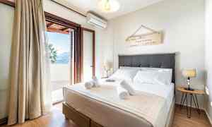 Et soveværelse med en dobbeltseng, dekorativt vægskilt, sengelamper og en åben balkondør der fører ud til en terrasse. (AI-genereret tekst)