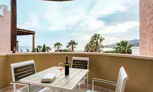 Udsigt fra en terrasse med bord og stole, vinflaske og glas. (AI-genereret tekst)