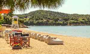 En sandstrand med liggestole og borde, med grønne bakker i baggrunden. (AI-genereret tekst)